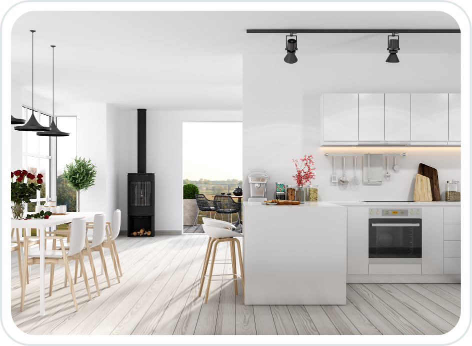 Modern white kitchen with open layout, black wood stove, white dining table with chairs, potted plants, and large window with views of greenery.
