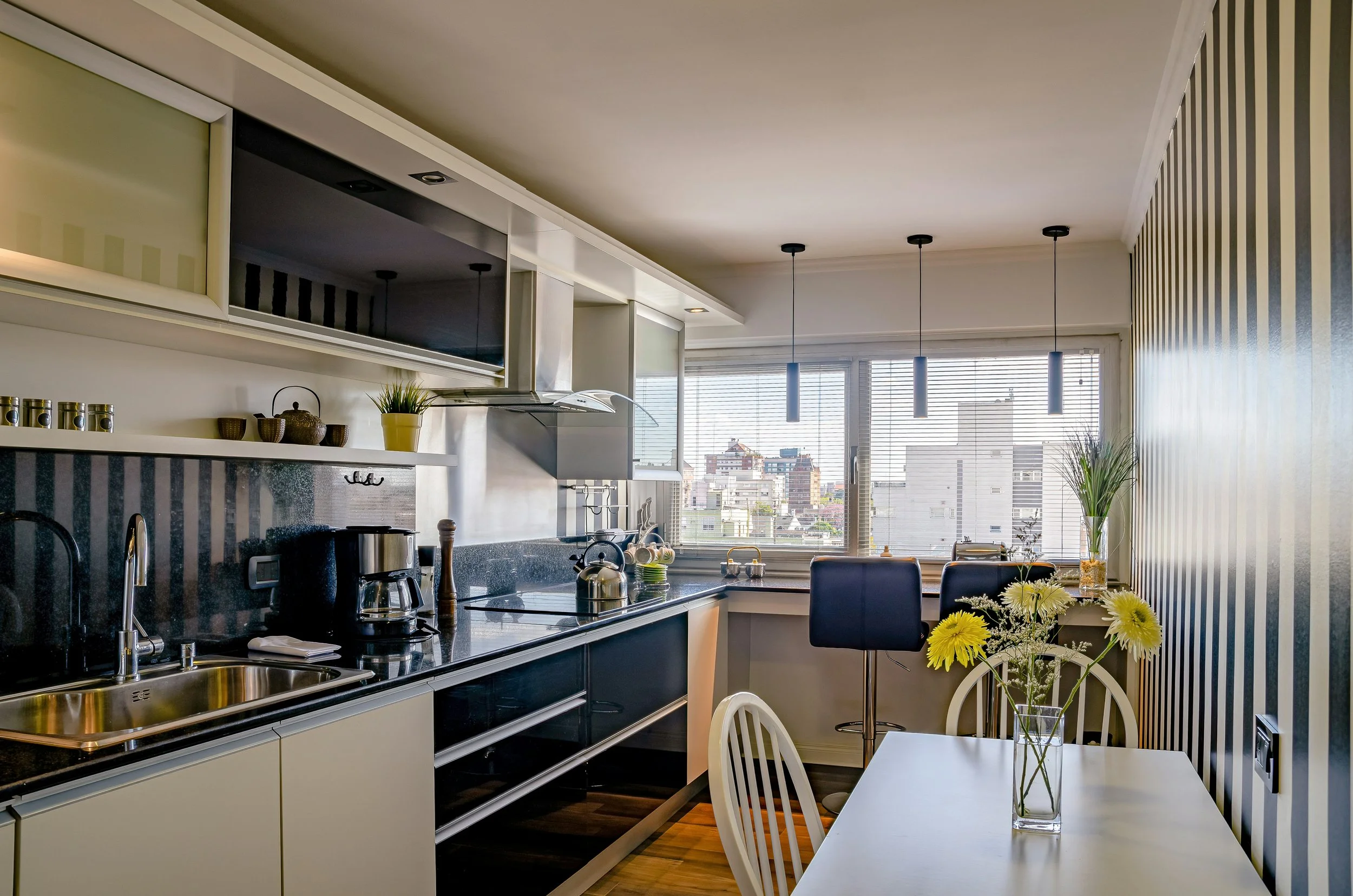 Modern kitchen with black and white cabinets, a small table with a vase of yellow flowers, and a window with city view
