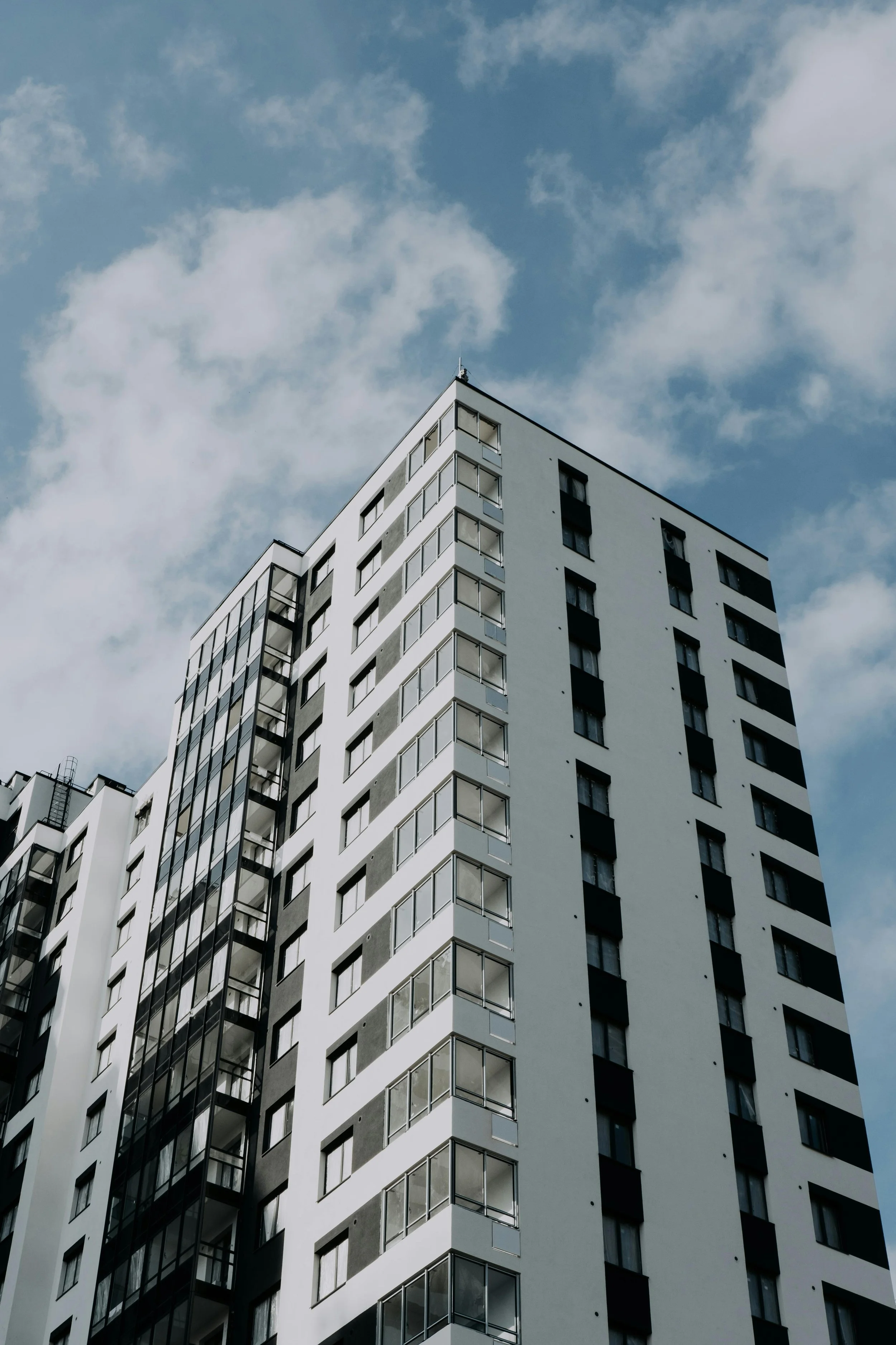 Low-angle view of a modern high-rise apartment building against a partly cloudy sky.