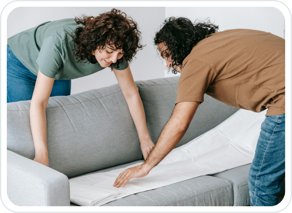 Two people making a sofa bed, one woman and one man, both with curly hair and smiles, working together in a bright room.