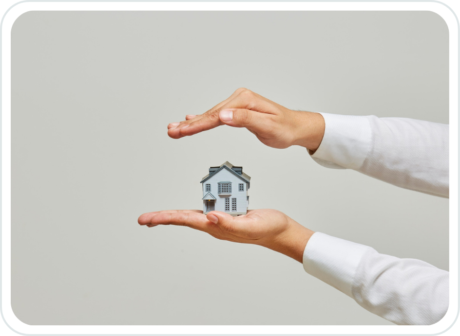 Person holding a small model house with both hands, one hand above and one below, against a plain background.