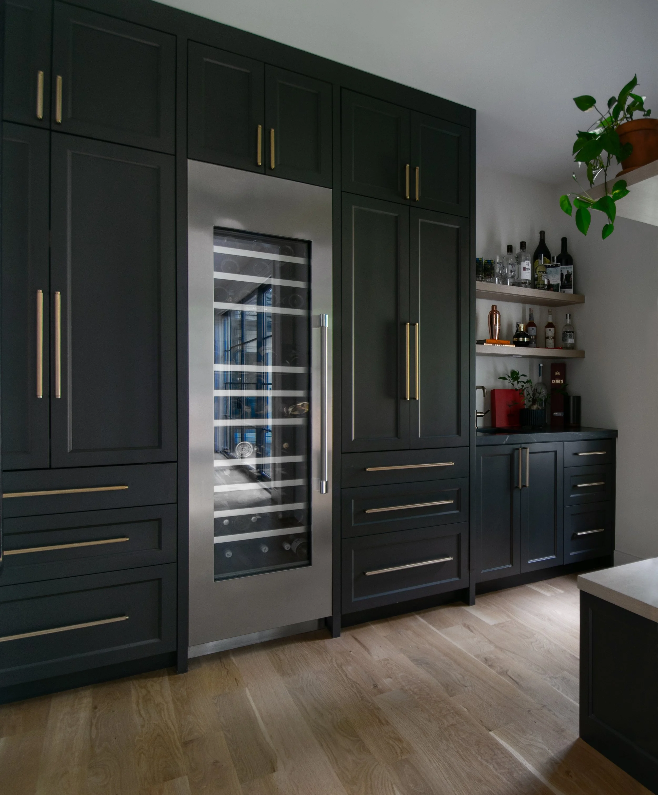 Luxury pantry designed by Erica Kay Design & Remodeling, featuring dark shaker cabinets with pocket doors, integrated wine fridge, wet bar with sink and floating shelves.