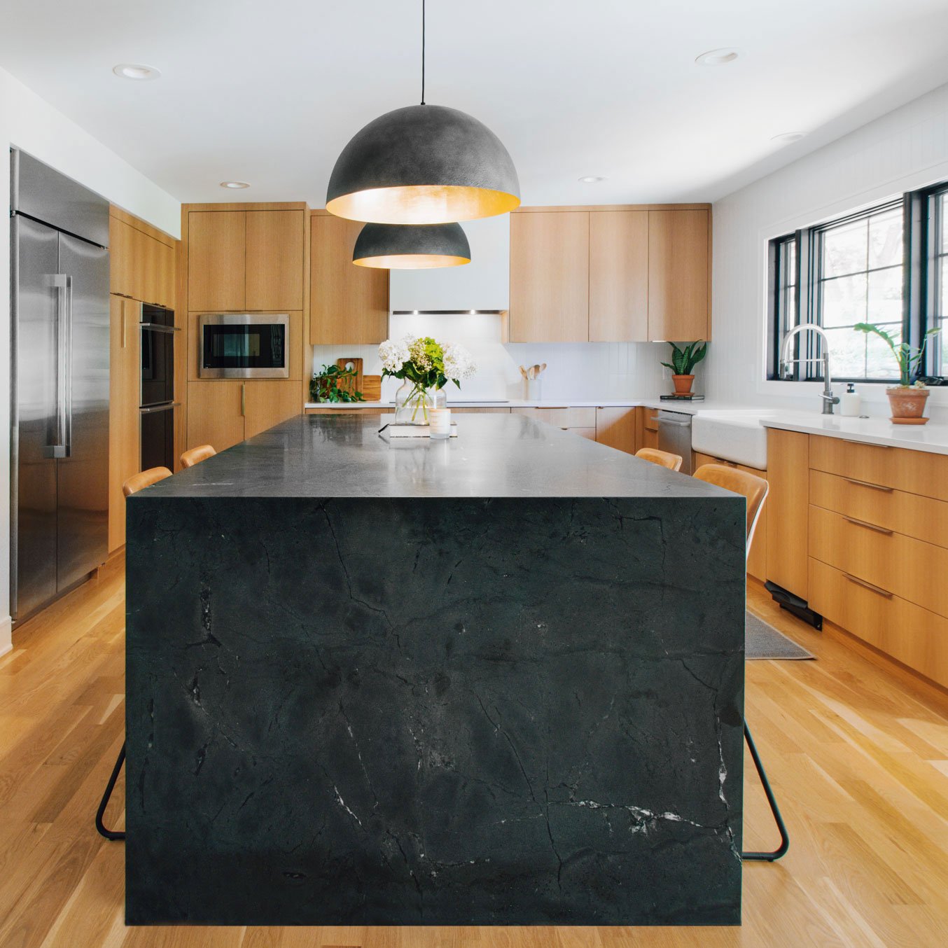 Kitchen renovation in Old Leawood, Kansas featuring custom white oak cabinetry, a dramatic waterfall stone island, integrated appliances, and modern lighting by Erica Kay Design & Remodeling.