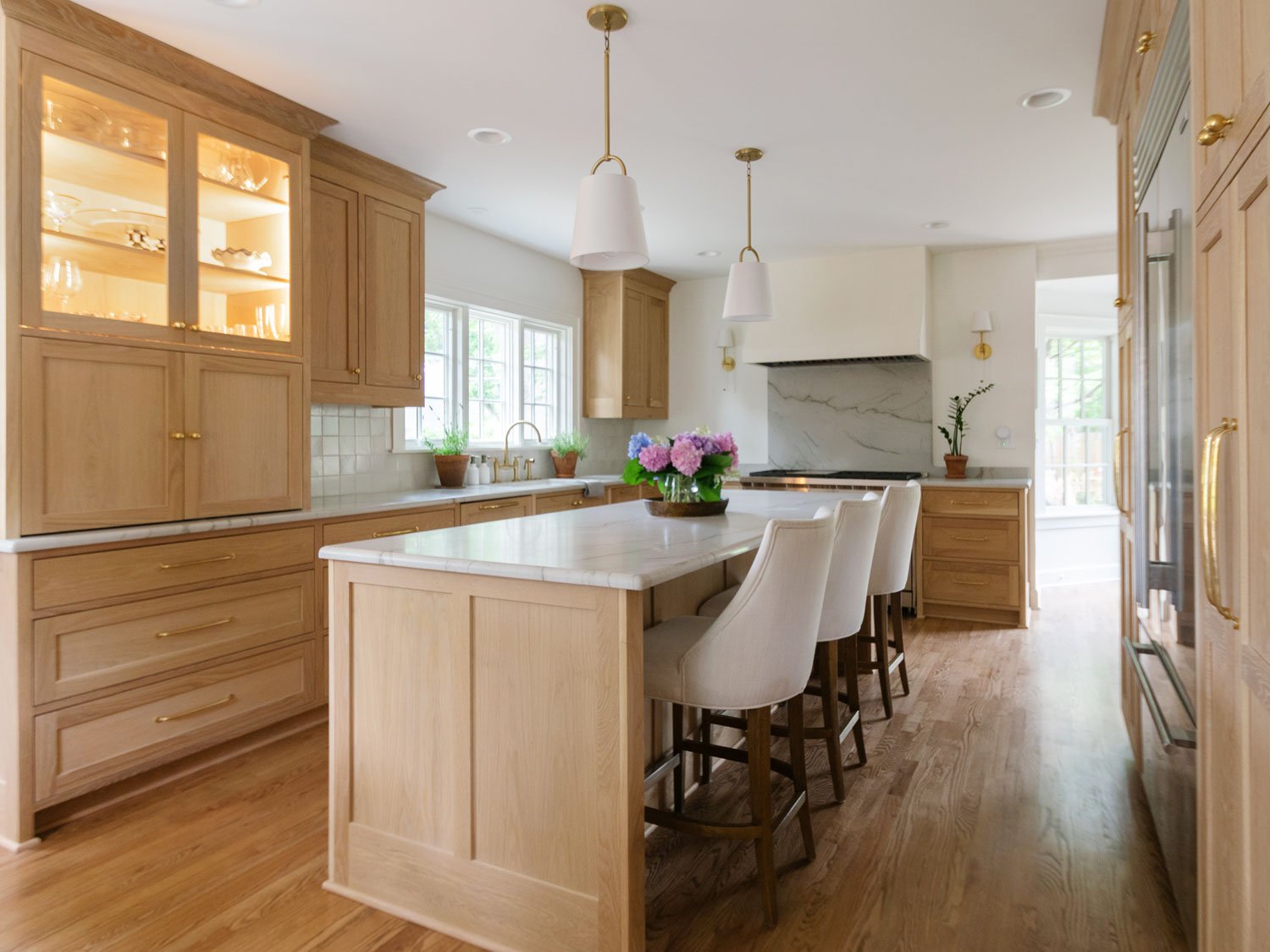 Brookside kitchen with inset white oak cabinetry, island seating, honed Luca di Luna countertops, and a custom plaster hood.