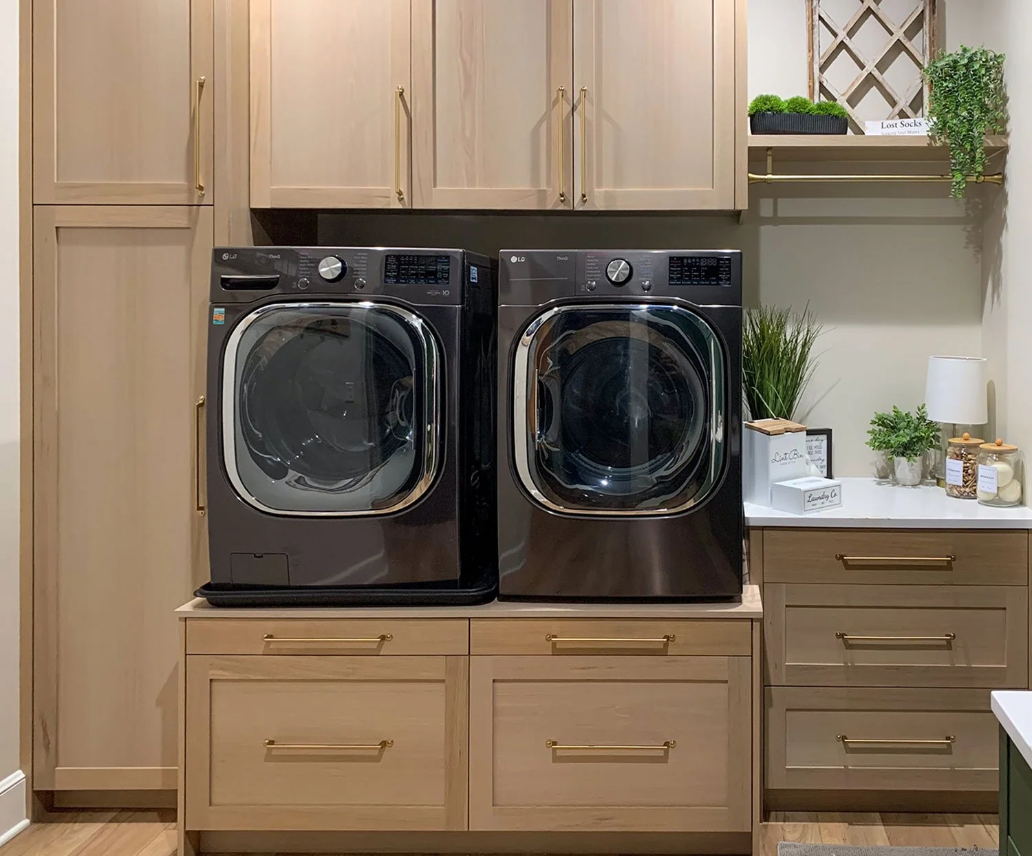 Custom laundry room remodel in Liberty, Missouri, by Erica Kay Design & Remodeling featuring a modern washer and dryer set integrated with light white oak cabinetry, a white quartz countertop, and elegant brass hardware.