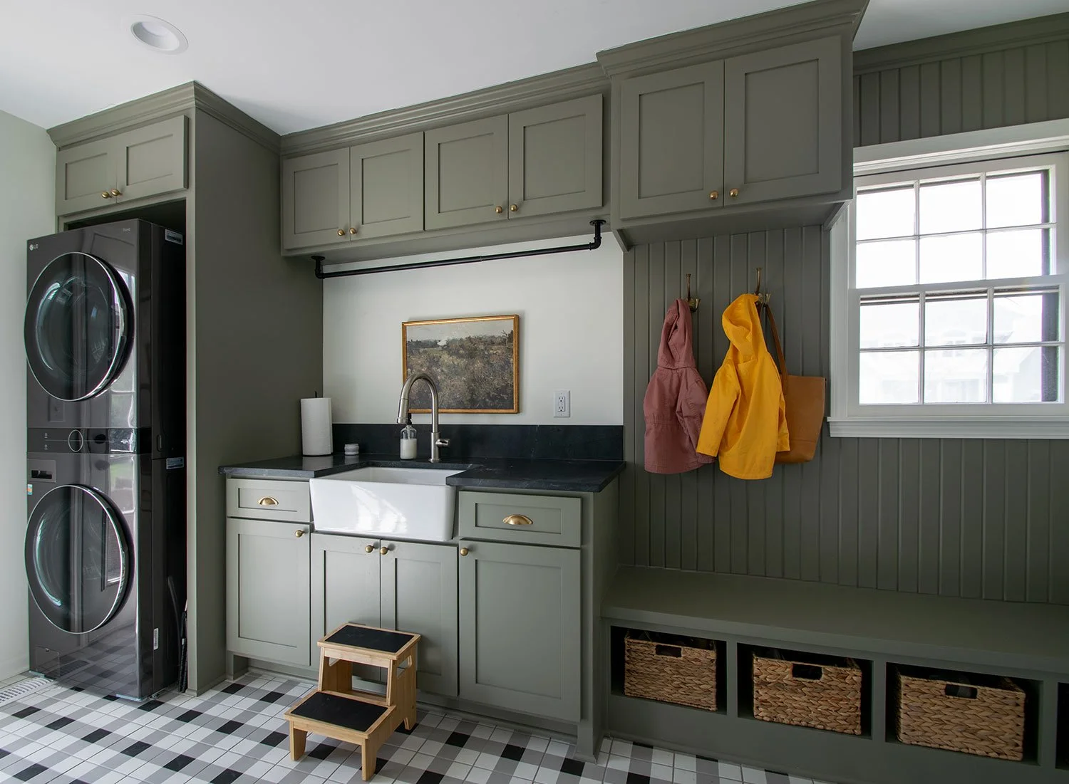 Modern laundry and mudroom remodel in Kansas City by Erica Kay Design & Remodeling, featuring custom olive green cabinetry, a white farmhouse sink, black soapstone countertops, and a built-in bench with cubbies and beadboard detailing.