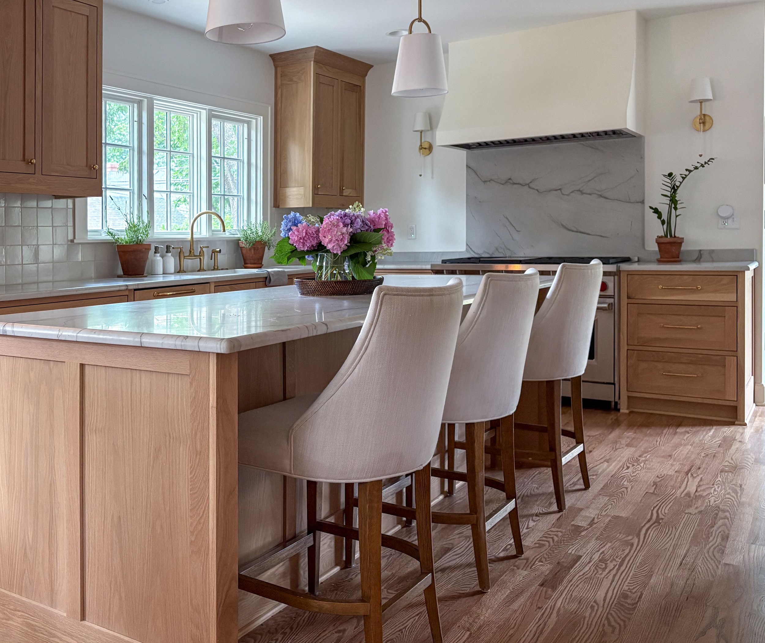 Brookside kitchen with inset white oak cabinetry, island seating, honed Luca di Luna countertops, and a custom plaster hood.