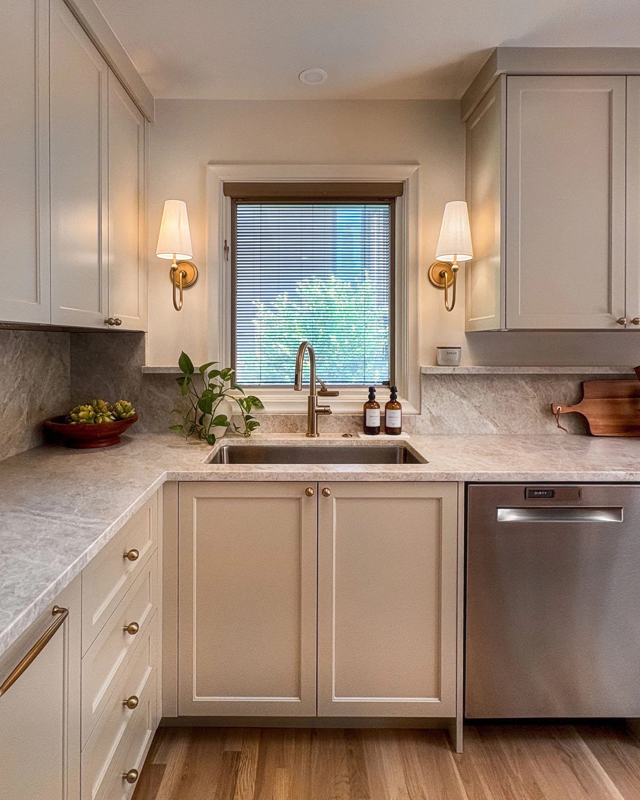 Kitchen sink beneath a window flanked by two shaded wall sconces.