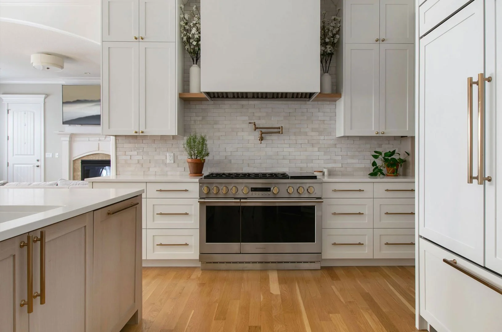 Completed luxury kitchen renovation in Kansas City by Erica Kay Design & Remodeling, featuring a professional 48-inch range, a custom white hood with wood mantle detail, a light grey zellige tile backsplash, and elegant brass hardware.