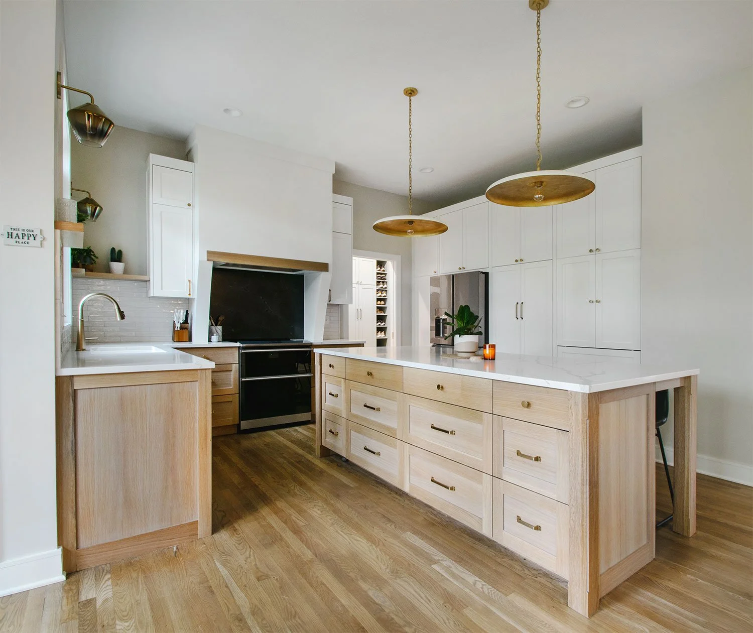 Transitional kitchen remodel in Overland Park, Kansas, by Erica Kay Design & Remodeling, featuring a large white oak island with marble countertops, white perimeter cabinetry, gold disc pendant lights, and a custom range hood with wood trim.