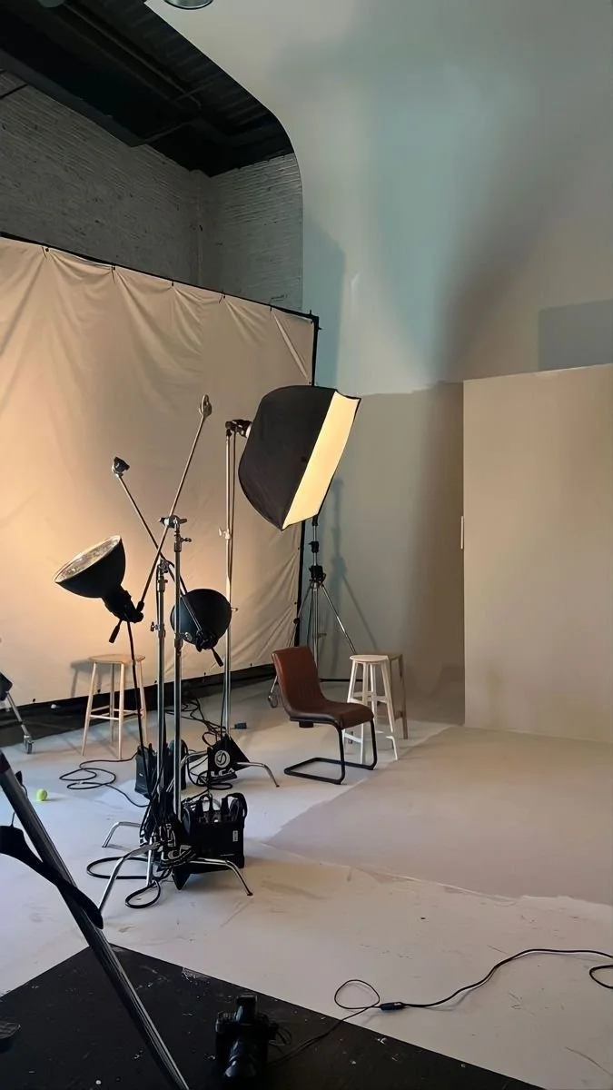 Estudio fotográfico con telón de fondo, iluminación profesional, varias lámparas y equipo de fotografía, dos sillas y un pequeño escenario.