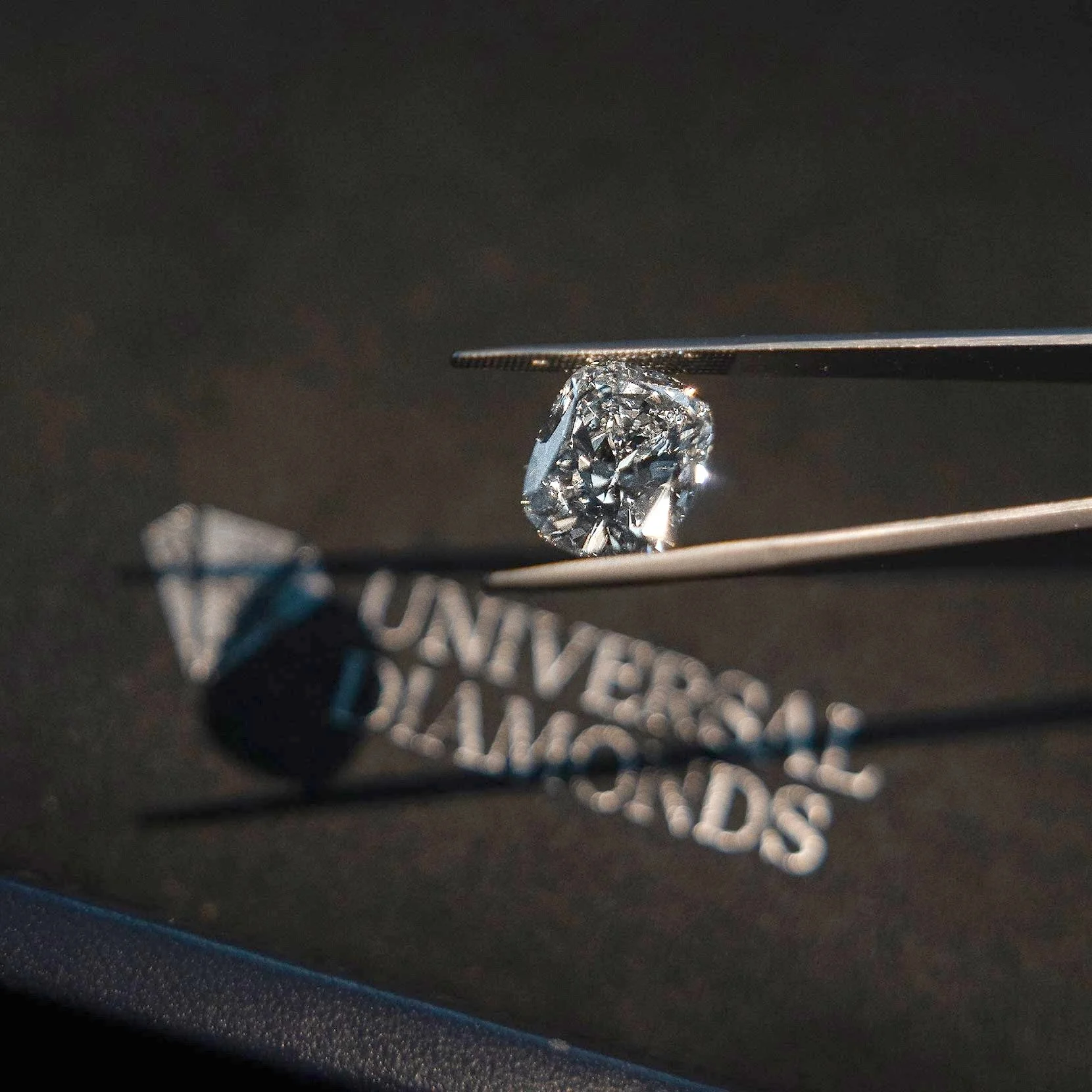 A close-up photo of a cut diamond held by tweezers, with a blurred background and a tag with partially visible text.