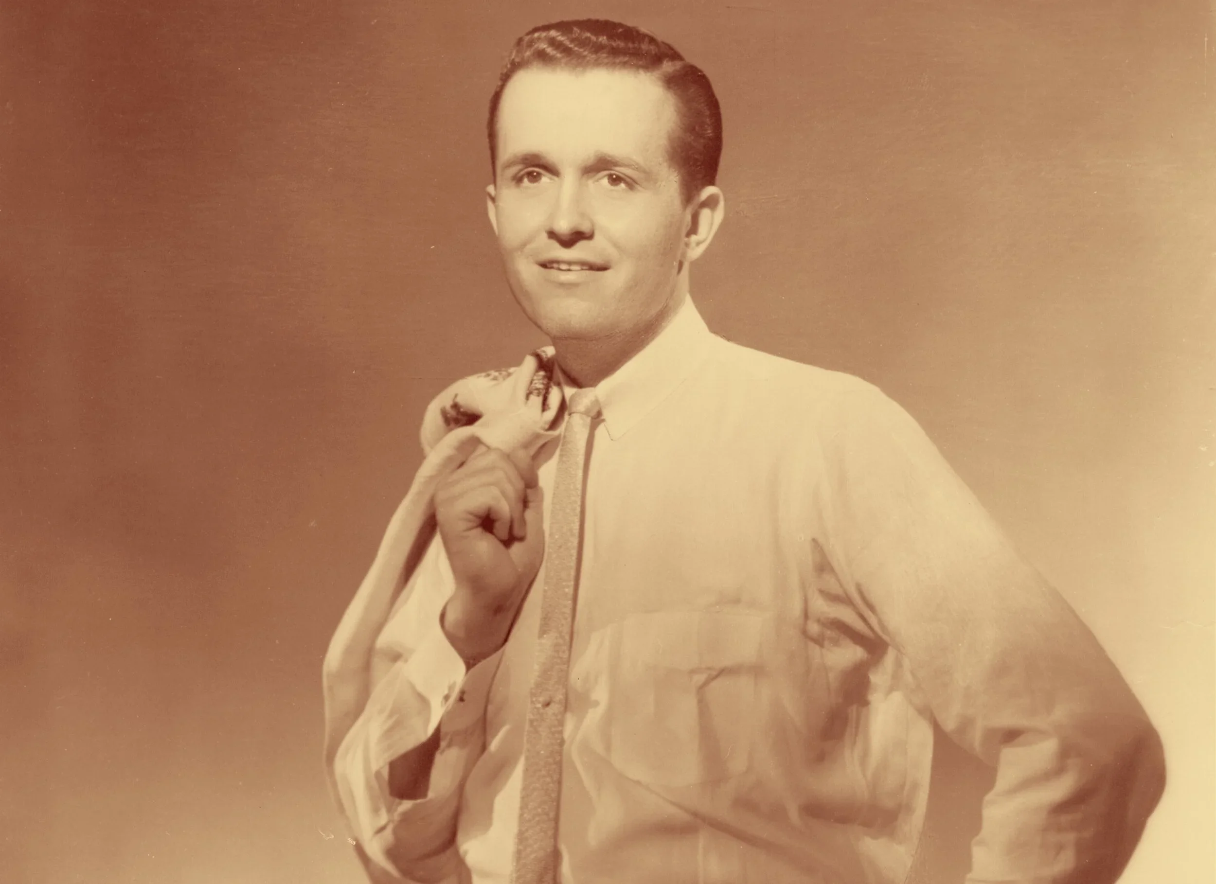 A vintage portrait of a young man with a retro hairstyle, wearing a light-colored suit, shirt, and tie, holding a necktie or scarf in his hand.