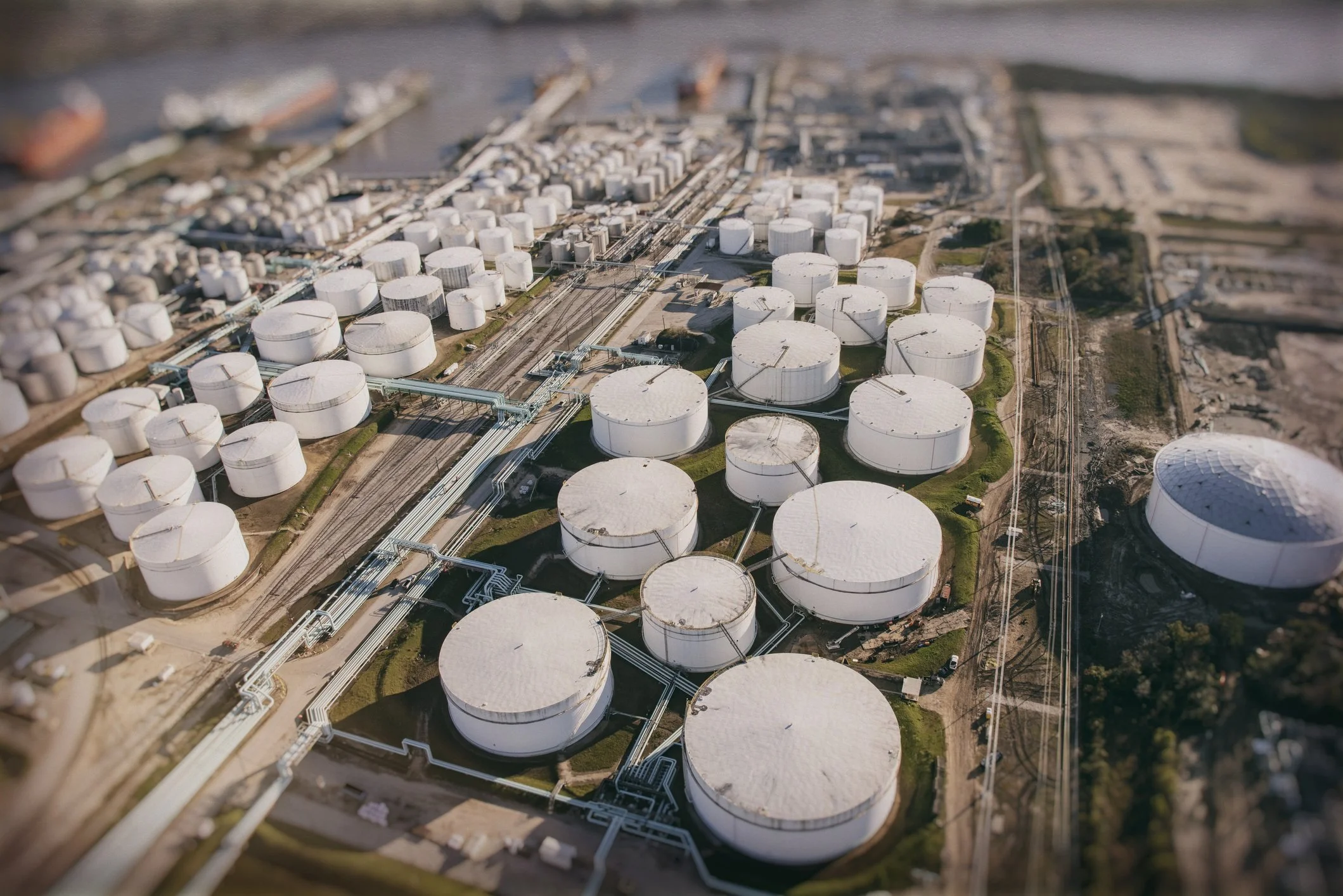 Aerial view of an industrial facility with numerous large white storage tanks connected by pipelines.