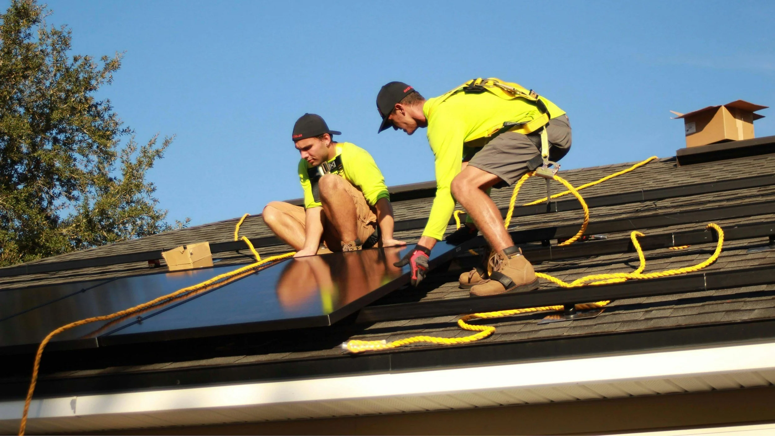 Two workers installing a solar panel on a roof on a clear day.