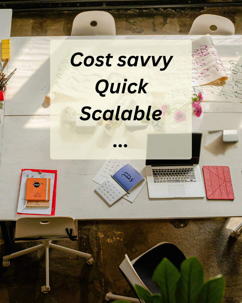 Overhead view of a workspace with a white table, laptops, notebooks, and stationery, with the overlay text 'Cost savvy, Quick, Scalable'.
