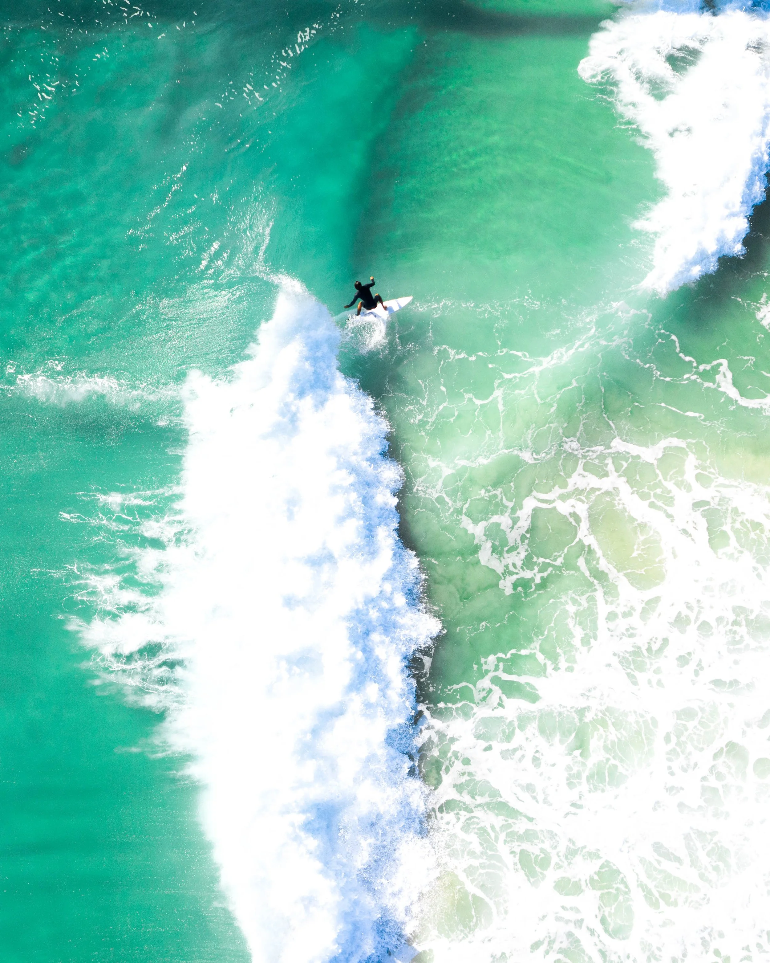 A dark wave, shot from above, being pulled in towards the shore.