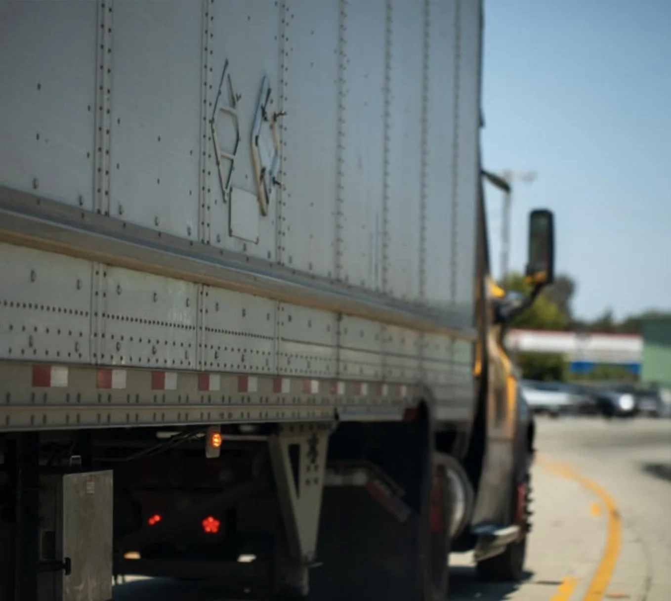 A semi-truck driving on a road with other vehicles and commercial buildings in the background.