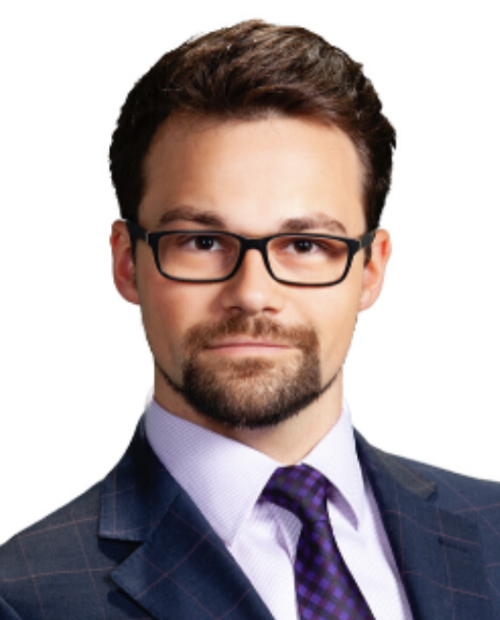 A professional man with glasses, wearing a suit and tie, looking directly at the camera with a neutral expression.