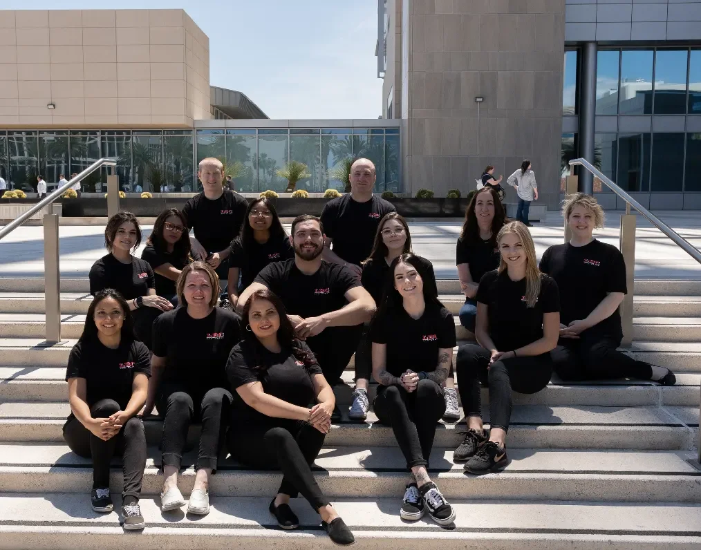 Group of people sitting and standing on outdoor stairs in front of a modern building, wearing black shirts.