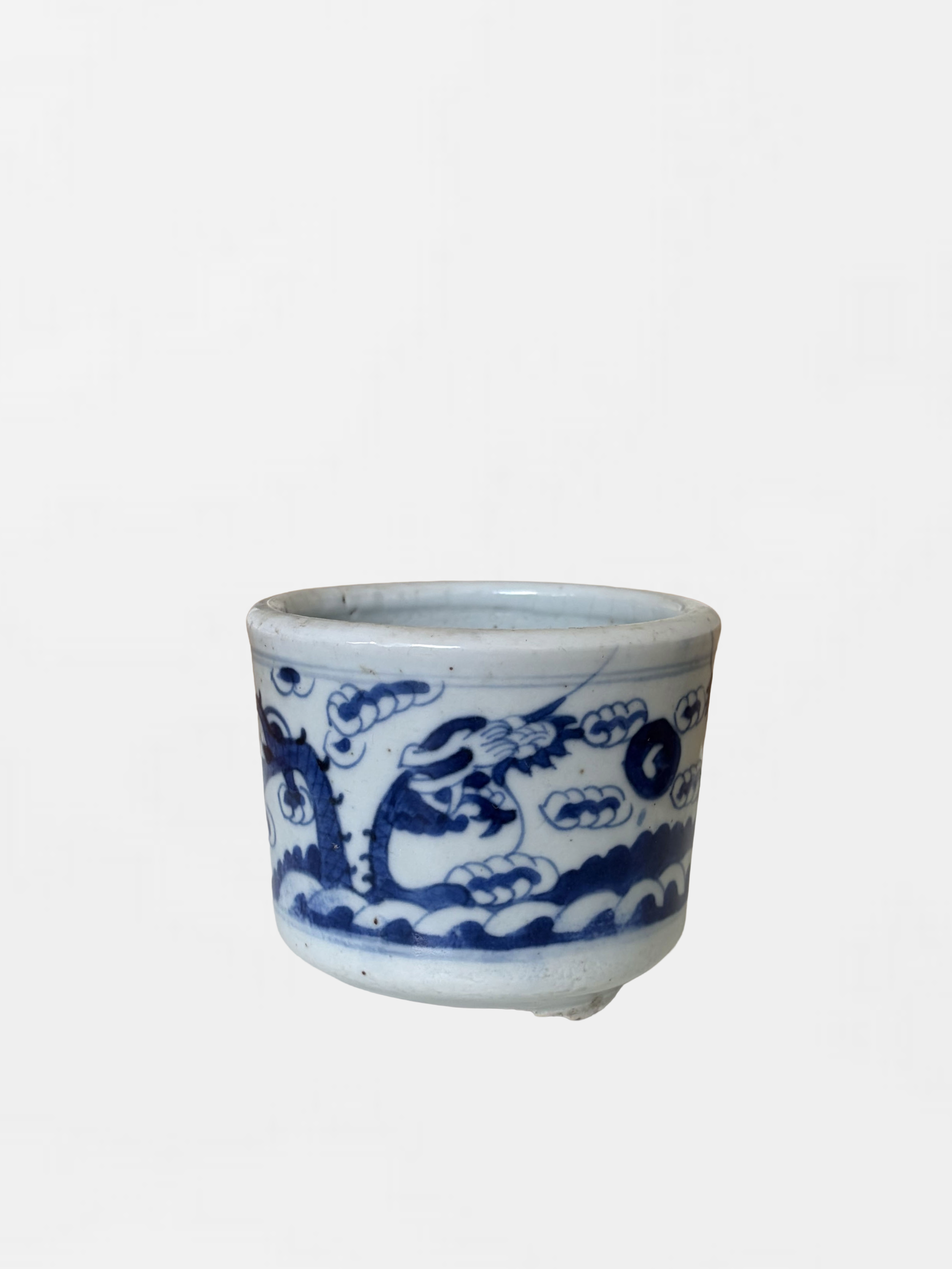 A porcelain cup with blue dragon and wave patterns on a white background.