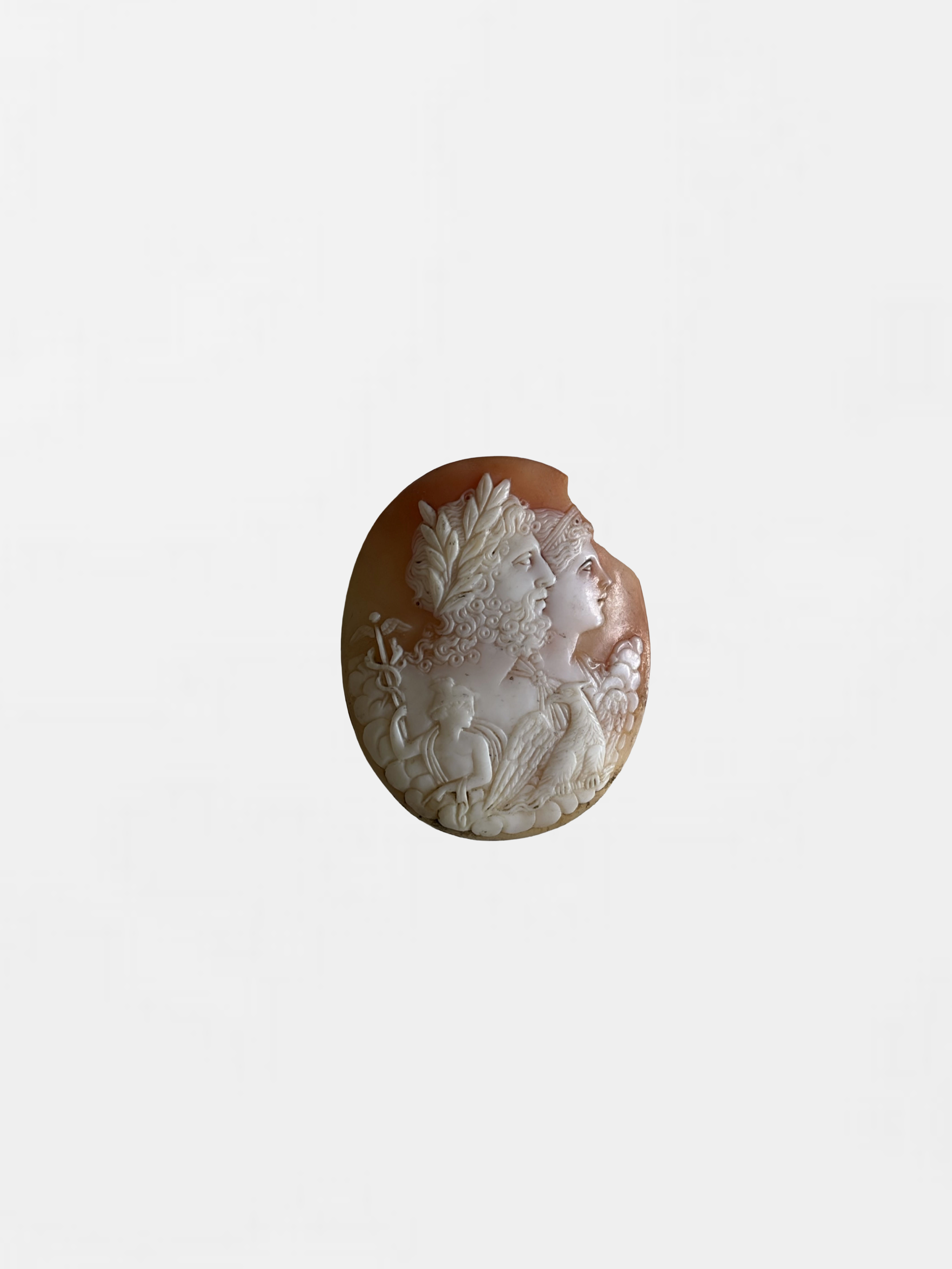A carved stone cameo featuring the profile of three women with intricate hair and clothing details, mounted on a plain background.
