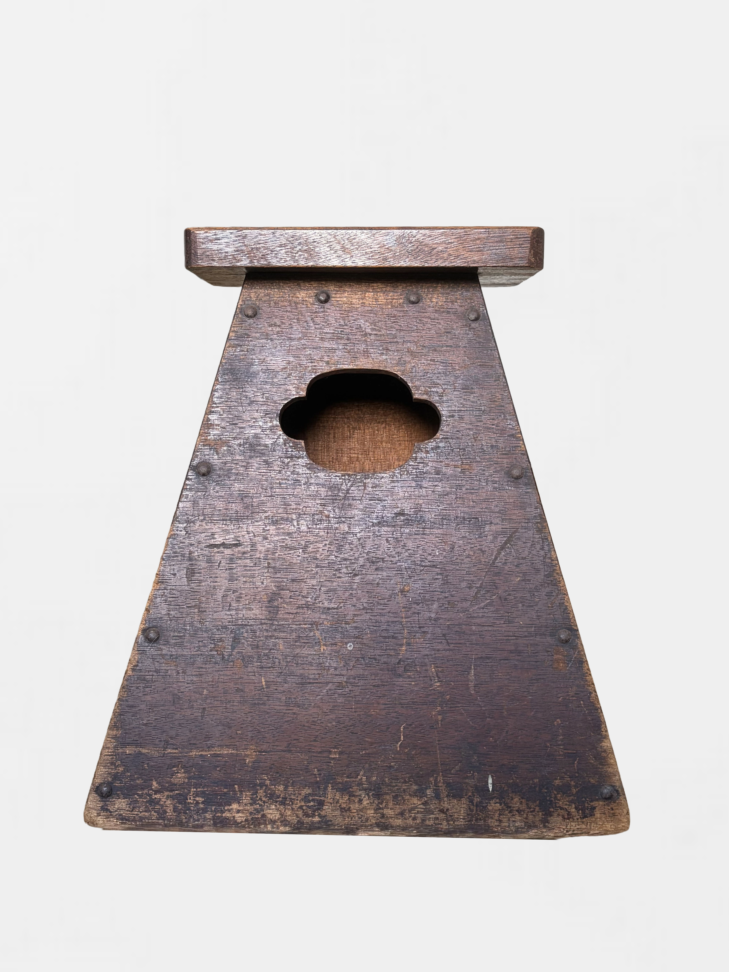 Close-up of a wooden stool with a four-leaf clover-shaped cutout in the center, showing a weathered dark brown surface against a plain light background.