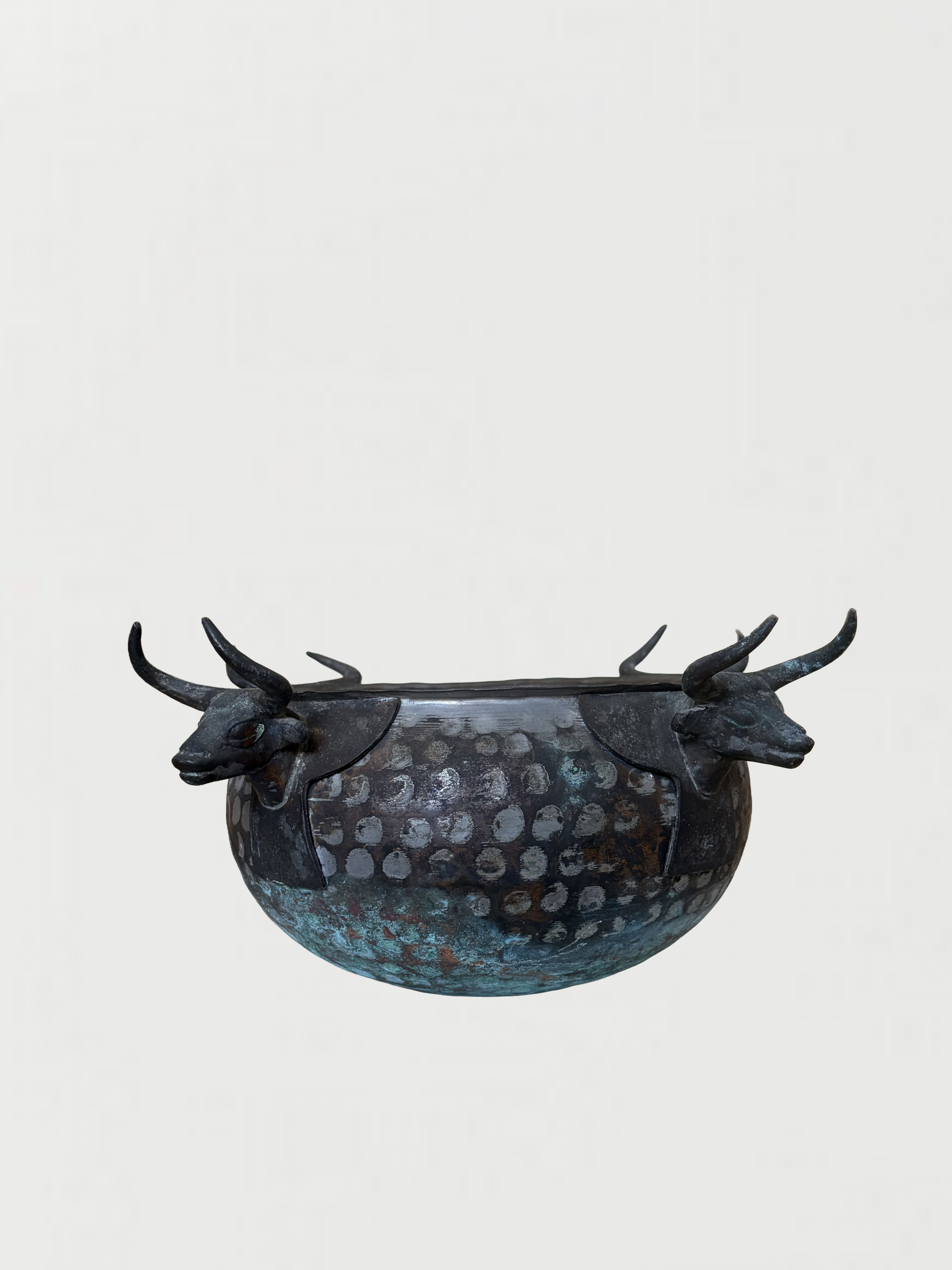 A metallic bowl with decorative animal heads on the rim, resembling stylized bulls or oxen, set against a plain white background.