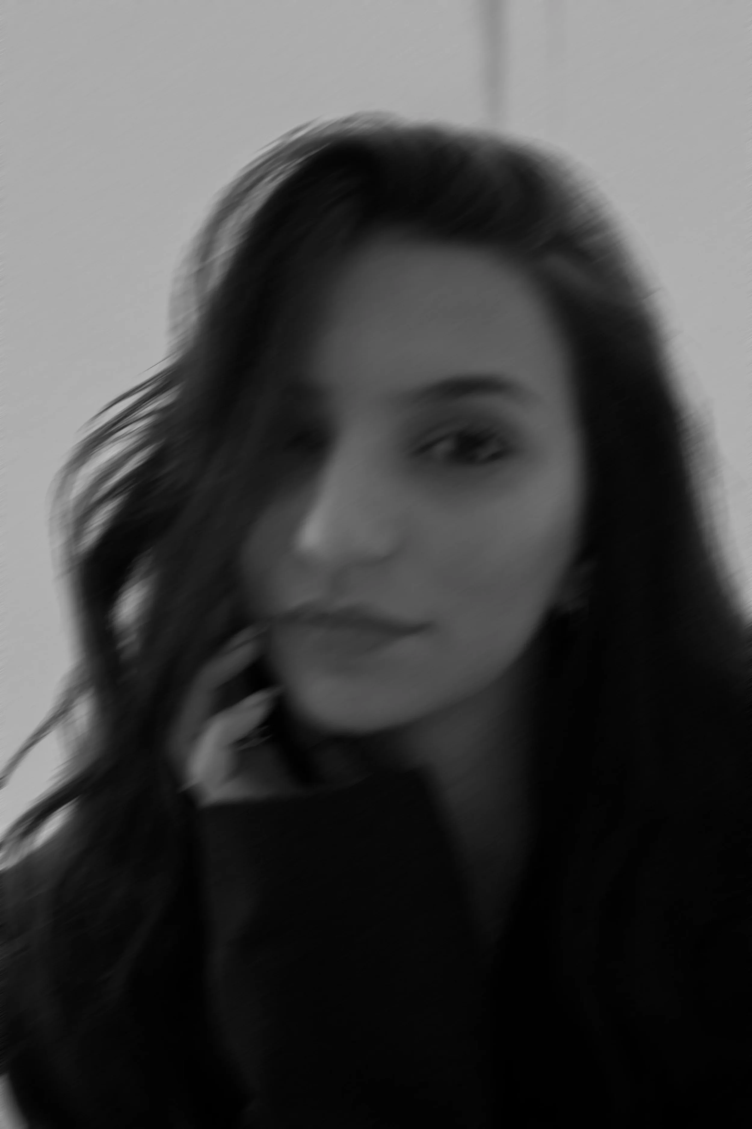 Photo floue d'une femme aux cheveux longs, portant un haut noir, avec une main près du visage.