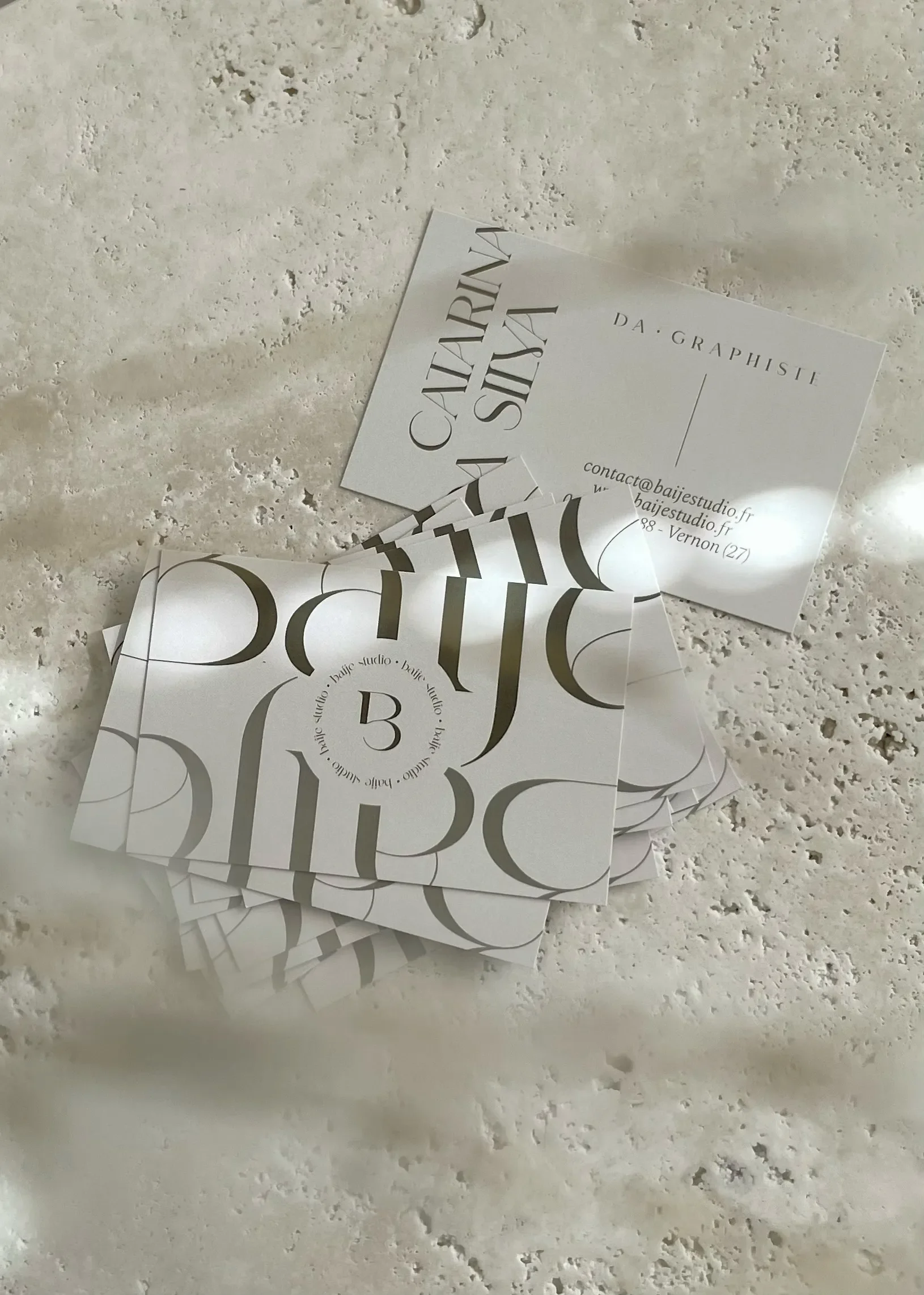 Cartes de visite blanches avec des caractères noirs, disposées sur une surface en pierre ou marbre, avec une partie pliée ou superposée.