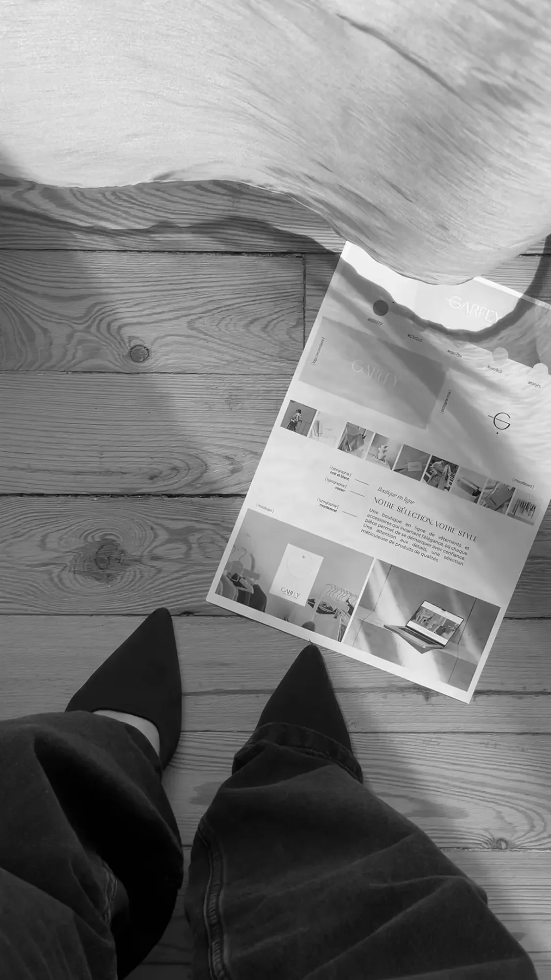 Photo en noir et blanc montrant la perspective d'une personne en chaussures noires, avec un brandboard sur un sol en bois.