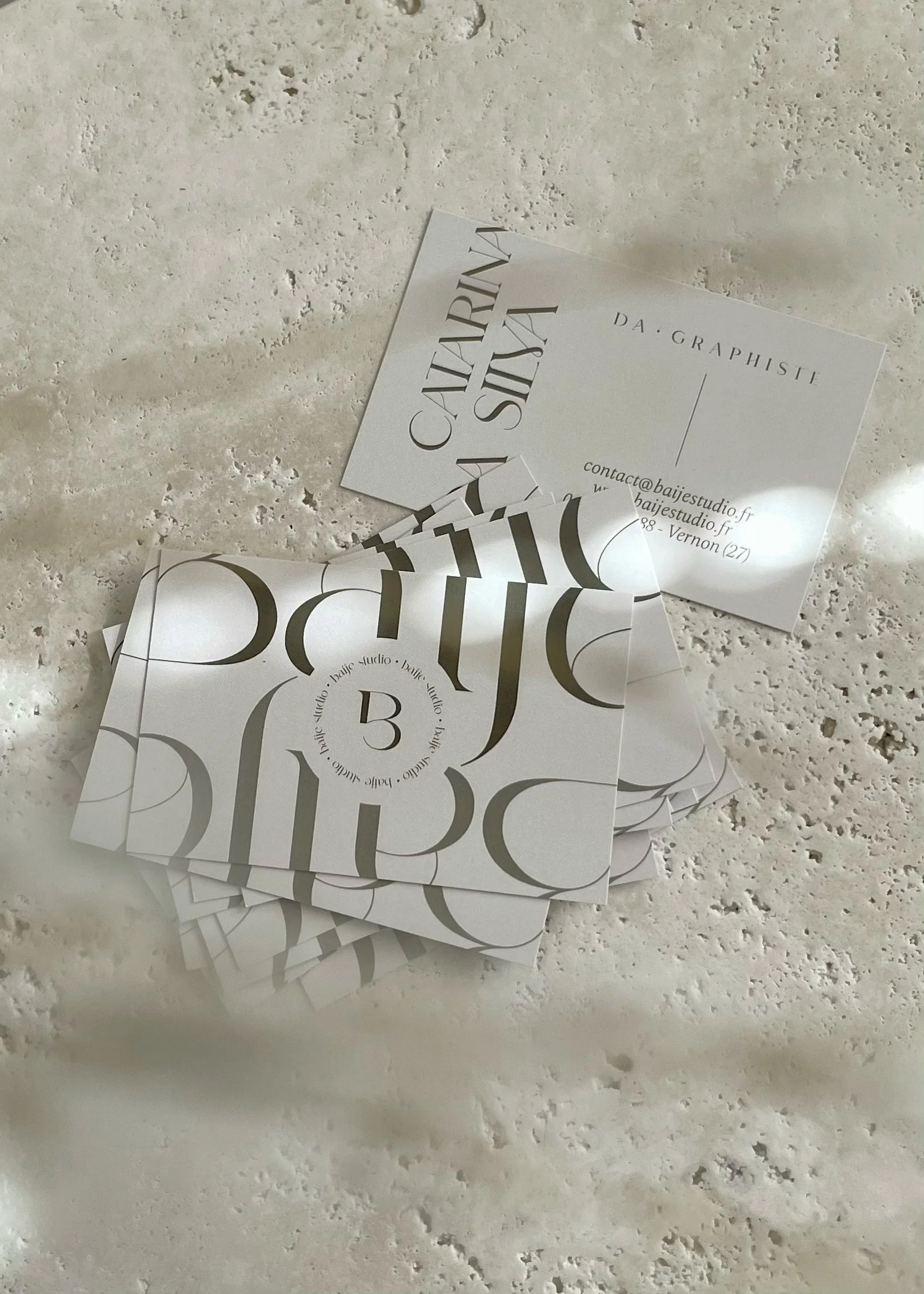 Cartes de visite blanches avec des caractères noirs, disposées sur une surface en pierre ou marbre, avec une partie pliée ou superposée.