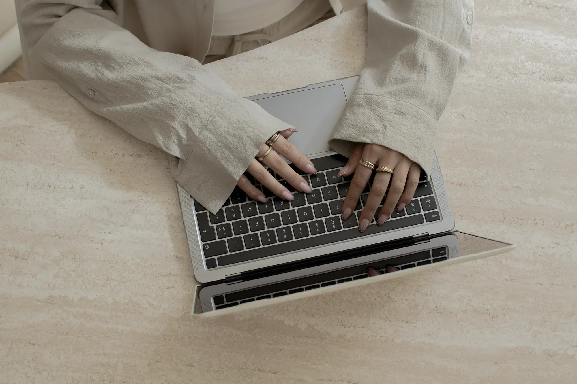 Les mains d'une personne en chemise beige utilisant un ordinateur portable sur une table en pierre