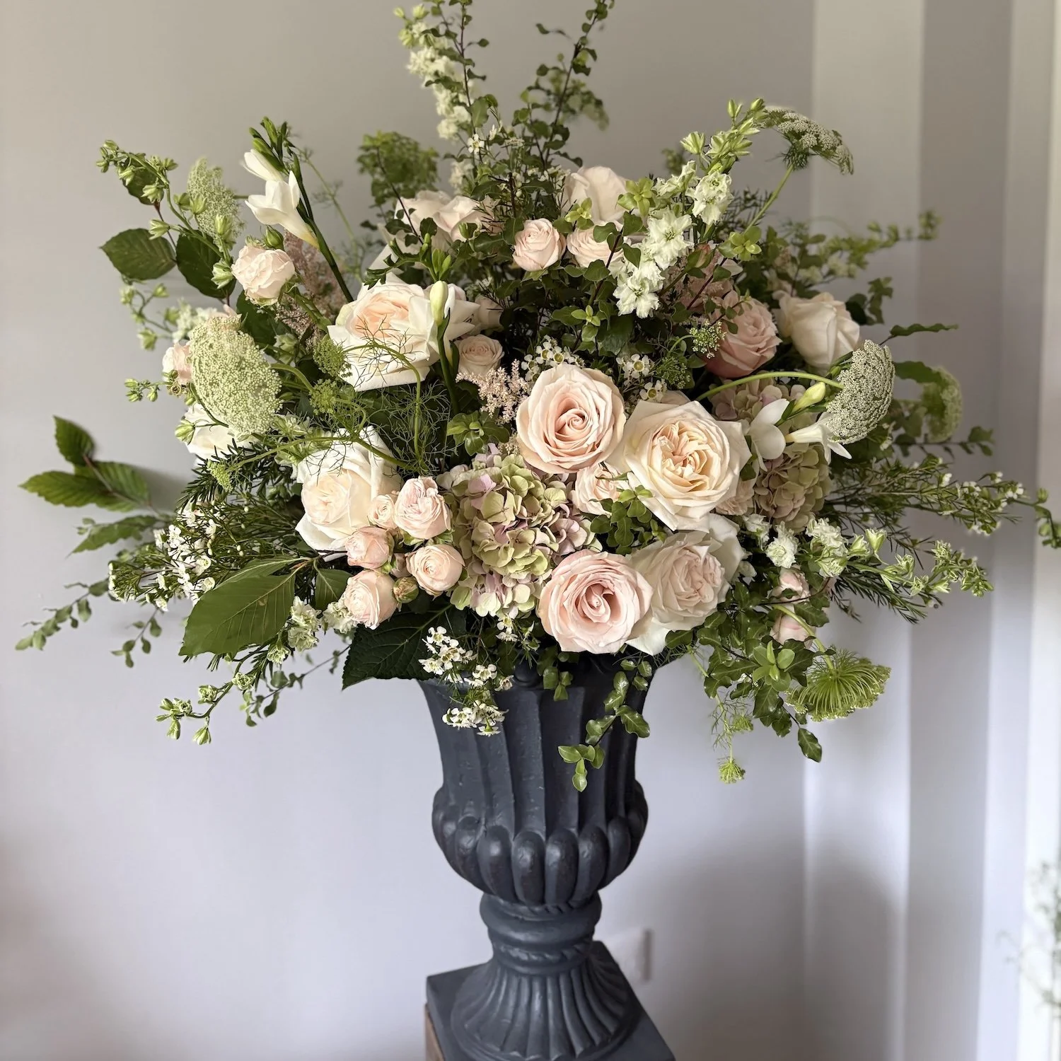 A large floral arrangement in a black decorative urn featuring pink and white roses, white lilies, and various greenery.