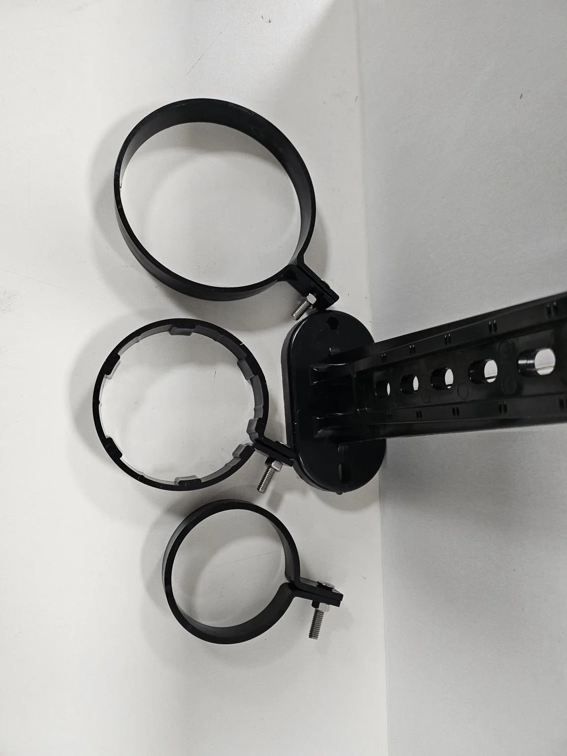 Disassembled black plastic mount with three circular rings, screws, and a mounting bracket on a white surface.