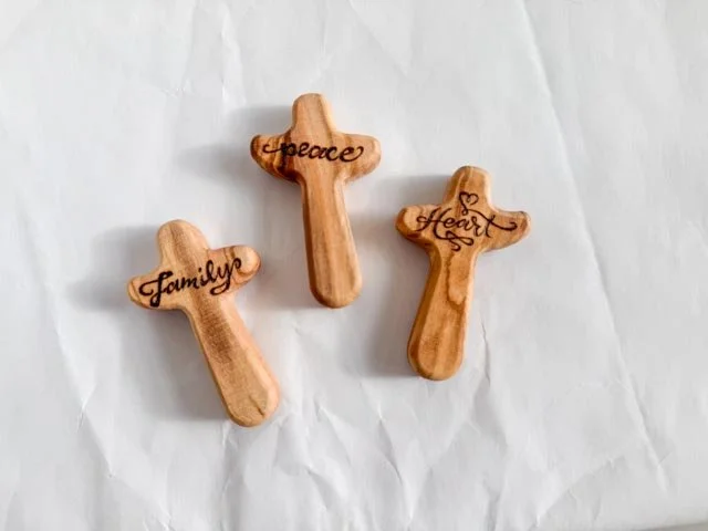 Three wooden personal pocket crosses with engraved words 'Family,' 'Peace,' and 'Heart' on a white background perfect for faith based gifts.