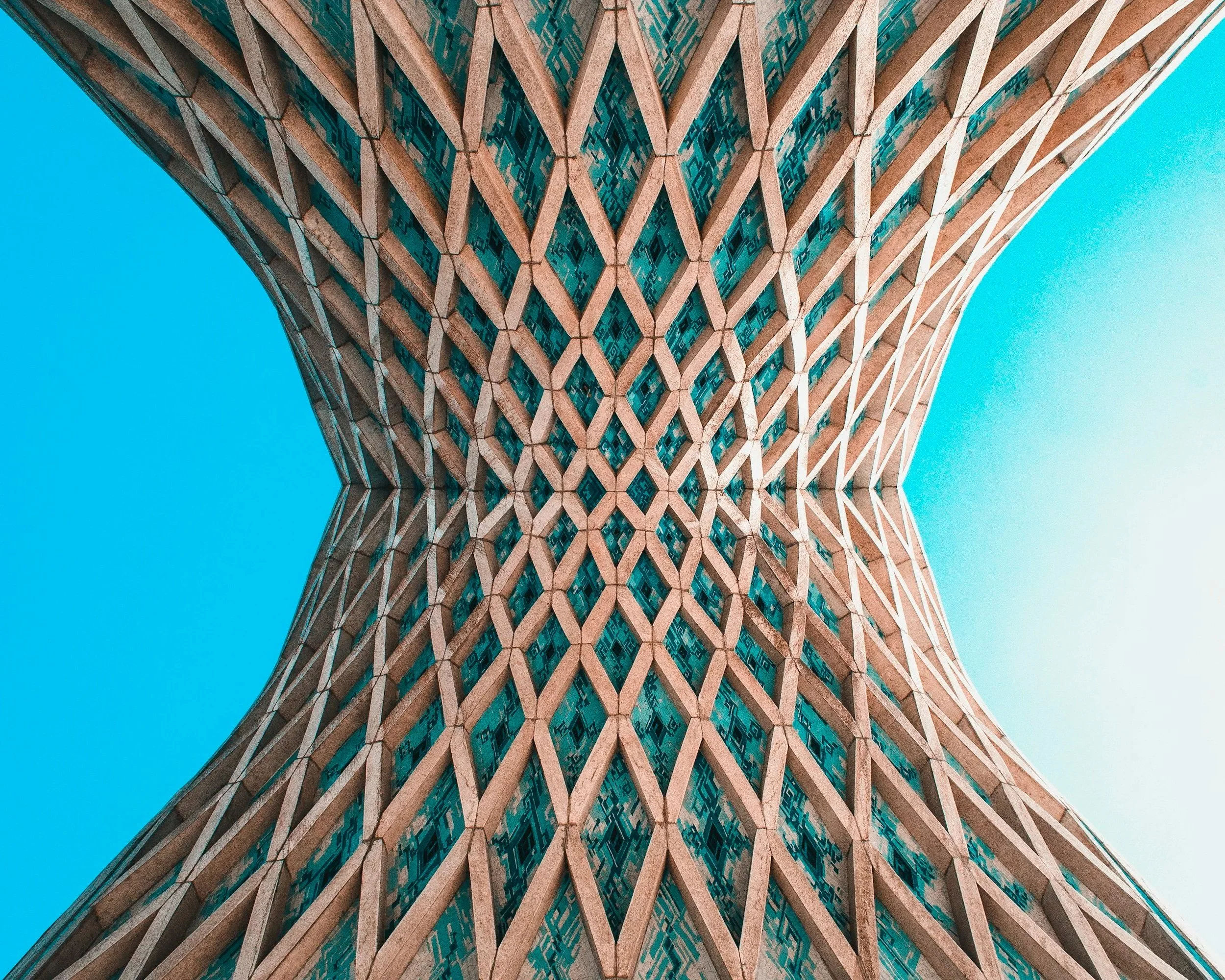 Looking up at a modern skyscraper with a unique, curving lattice pattern on its facade, set against a bright blue sky.