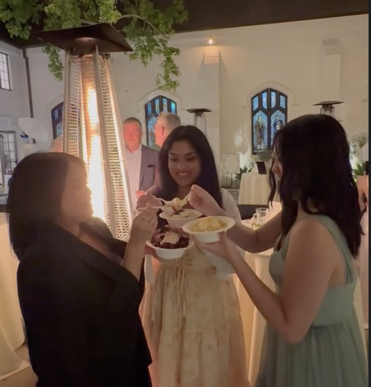 Three women sharing bowls of Korean shaved ice at a social gathering indoors with a patio heater and decorative windows in the background.