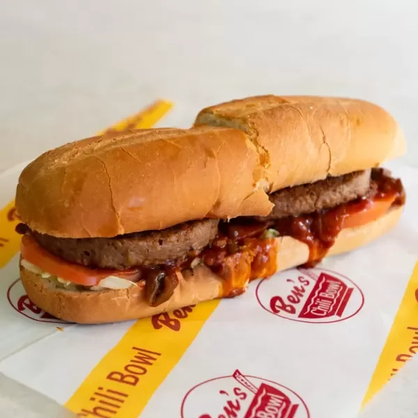 Close-up of a cheeseburger with onions, tomato, ketchup, and mayonnaise in a bun, on Ben's Custom Burgers branded paper