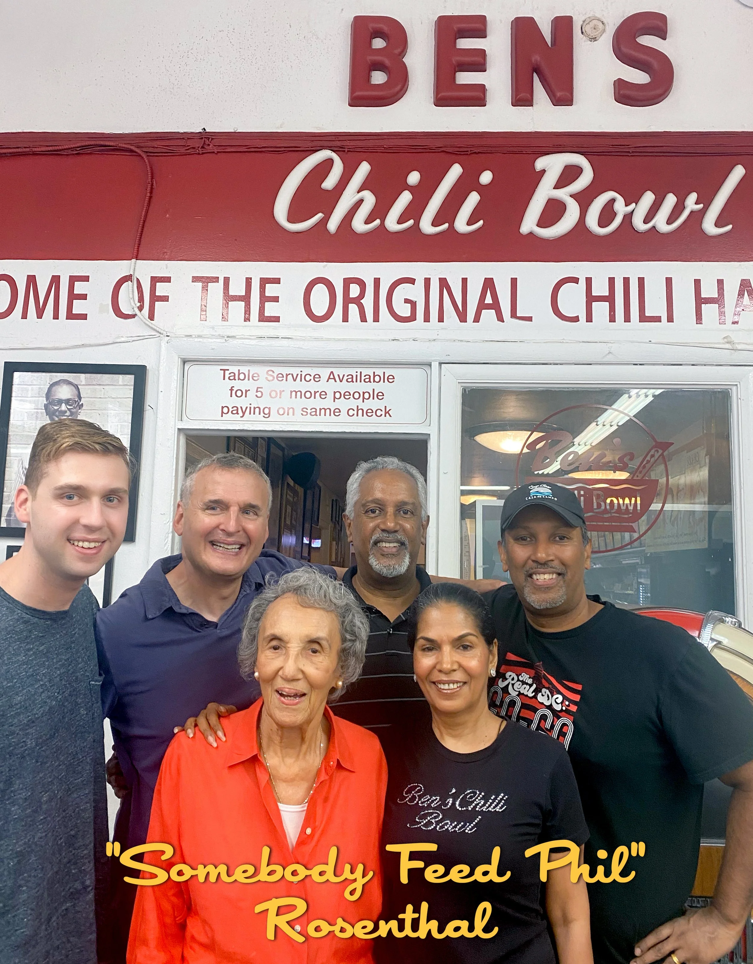 Group of six people inside Bens Chili Bowl restaurant, smiling for a photo. The restaurant sign reads 'Bens Chili Bowl,' with a slogan 'Somebody Feed Phil' Rosenthal written across the bottom of the image.