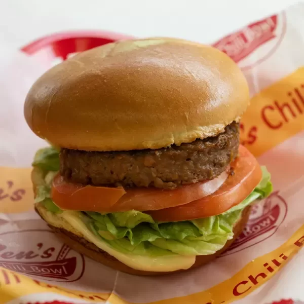 Close-up of a cheeseburger with lettuce, tomato, and a beef patty in a bun, on fast food restaurant paper.