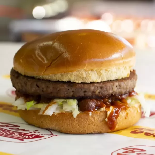 Close-up of a cheeseburger with a shiny bun, beef patty, lettuce, and barbecue sauce.