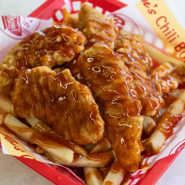 Fried chicken pieces covered in barbecue sauce served over French fries in a red and white food tray.
