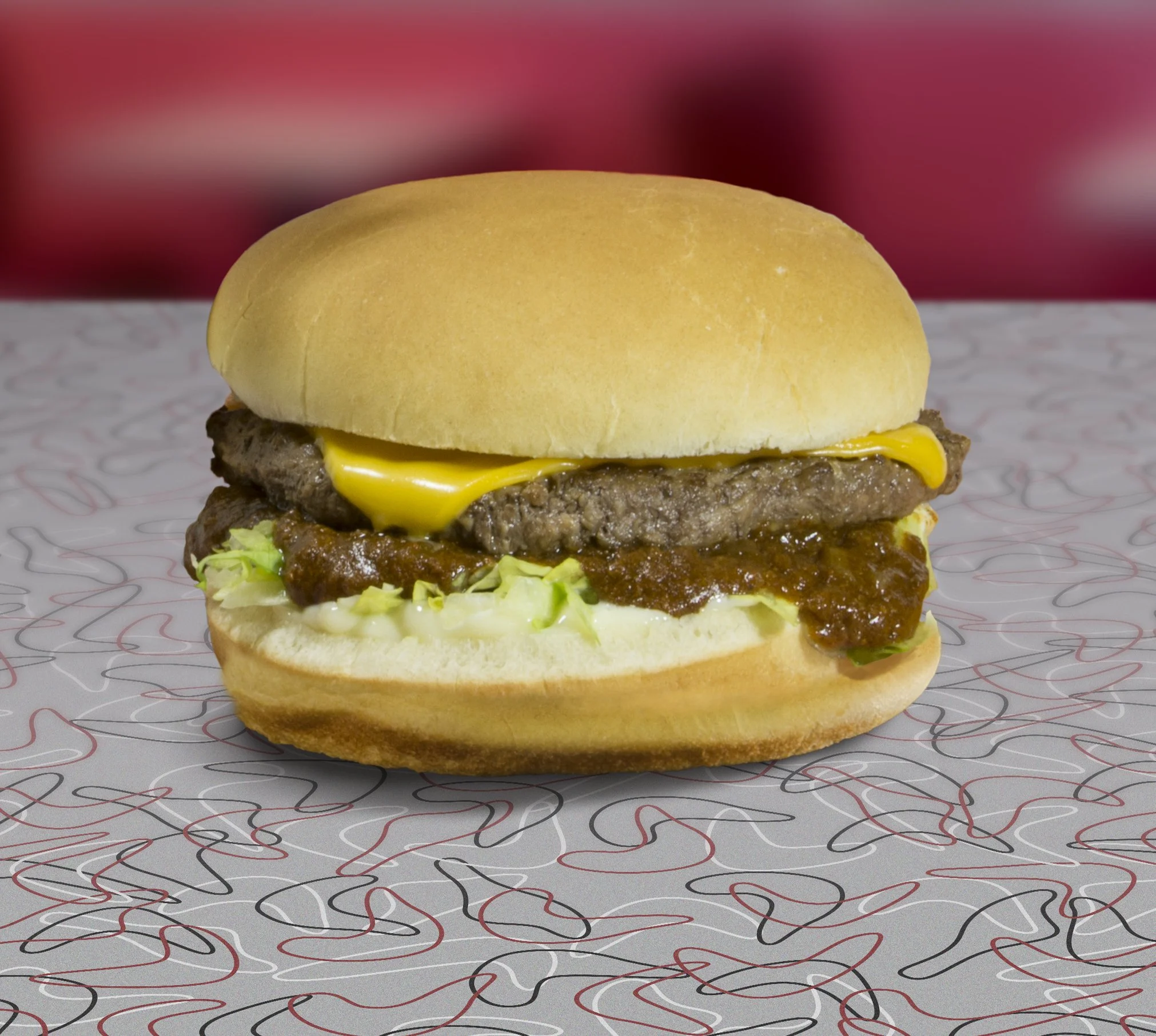 Beef cheeseburger with lettuce, tomato, cheese, and sauce in a soft bun on a patterned tray.