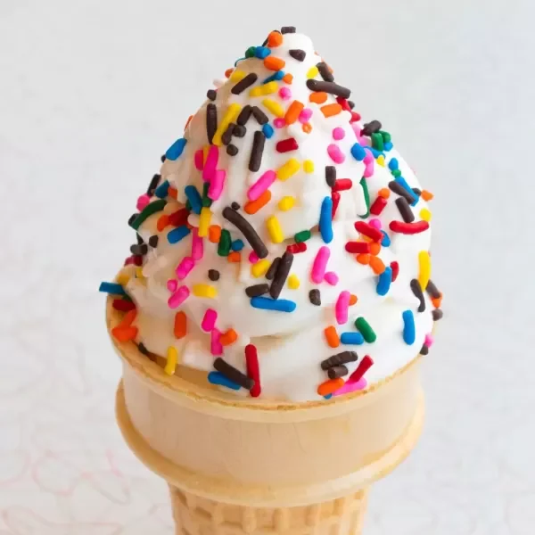 Ice cream cone topped with whipped cream and colorful sprinkles.