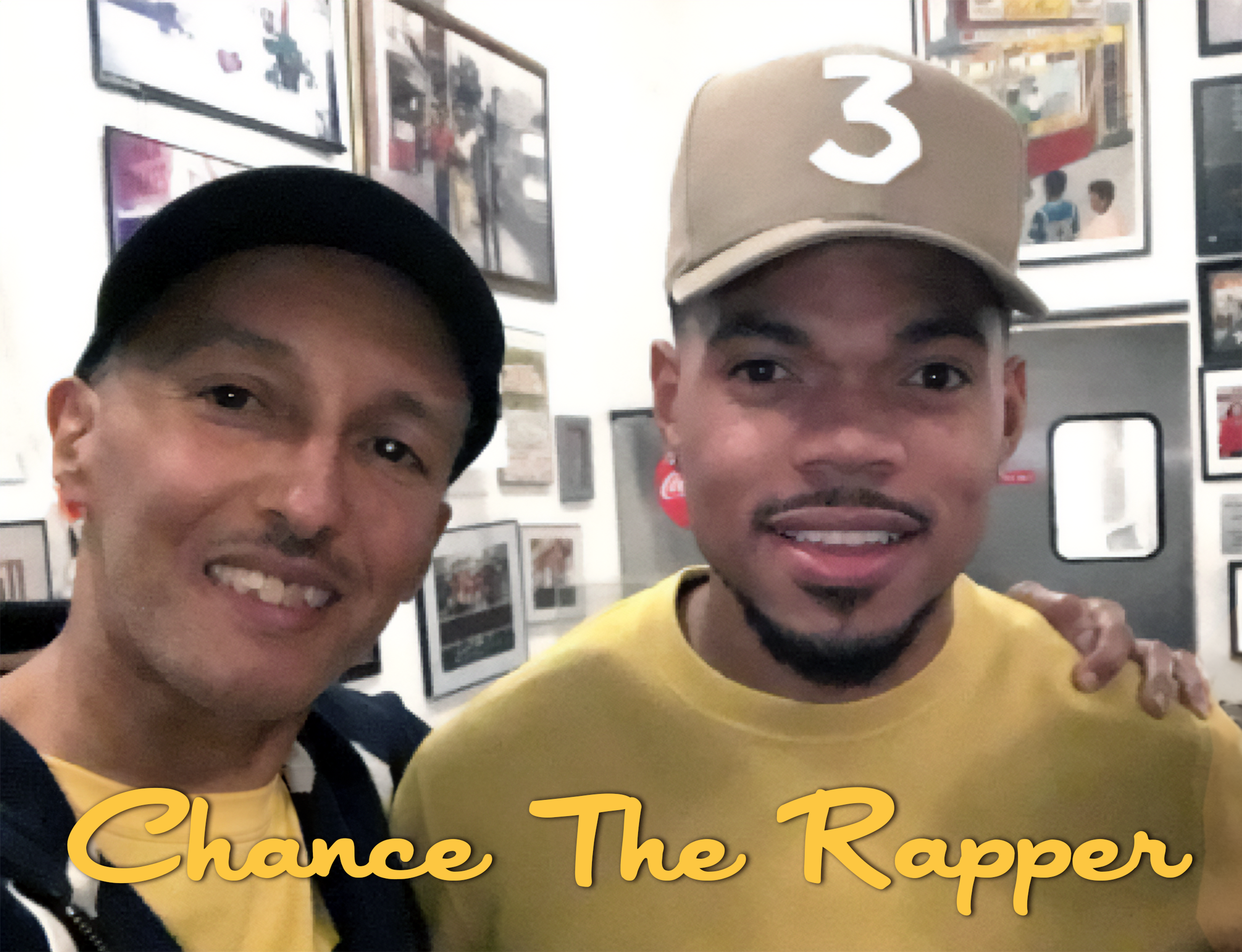 Two smiling men take a selfie in a room decorated with framed pictures on the wall. One man is wearing a black cap and black jacket over a yellow shirt, and the other man is wearing a beige cap with the number 3 and a yellow shirt. The text "Chance T