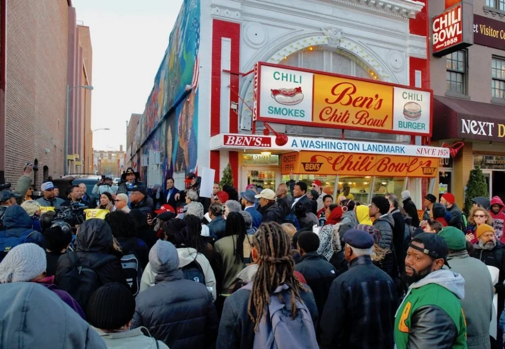 A crowd of people waiting outside Ben's Chili Bowl, a historic restaurant in Washington, D.C., known for chili and burgers, with signage and a colorful mural on the building.