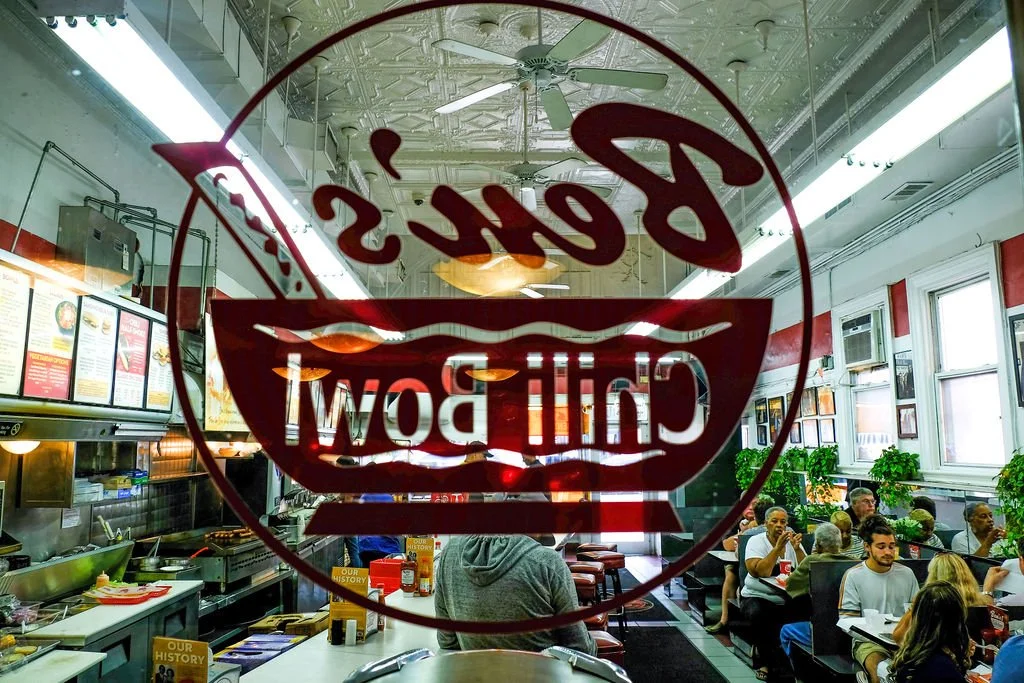 Inside a restaurant with a glass window displaying the restaurant's logo, showing a bowl and the words 'Bene's Chili Bowl'.