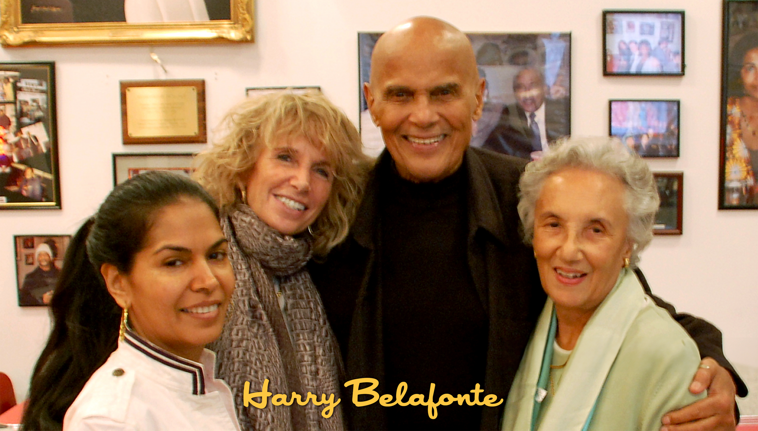 Four people smiling and standing close together in an indoor setting with framed pictures on the wall behind them, with 'Harry Belafonte' text overlaid.