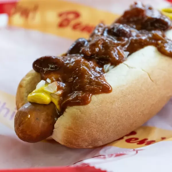 Hot dog in a bun topped with mustard and beef chili.